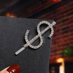 Close-up of a silver dollar sign hair clip with sparkling rhinestones held by a hand