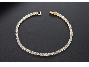 Detail view of a gold tennis bracelet featuring round zircons on a dark textured background