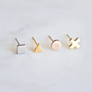 Minimalist geometric stud earrings set in gold and silver on marble background
