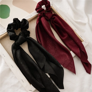 Detail of black and wine red satin scrunchies with long ribbons on white textured fabric
