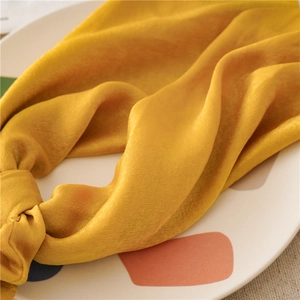 Macro shot of bright yellow satin hair scrunchie with knot detail and silky texture