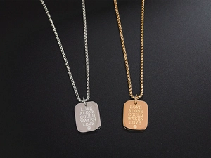 Macro view of gold and silver square pendants engraved with Love Alone Could Waken Love