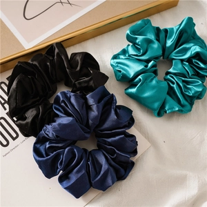Detailed view of large satin scrunchies in black, navy, and emerald on a wooden tray