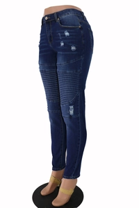 Detail view of blue distressed skinny jeans with ripped holes and knee pleats on a mannequin