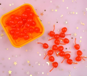 Close-up of bright red resin cherry charms for DIY crafts on a glittery background