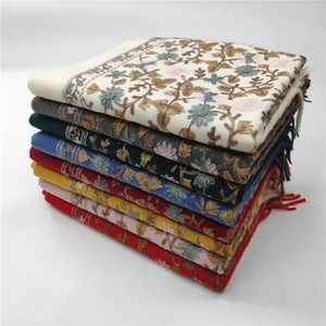 Close-up of stacked winter cashmere shawls featuring intricate floral embroidery and tassels