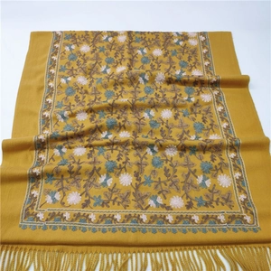 Detail of yellow cashmere-like scarf featuring intricate floral embroidery and tassel fringe