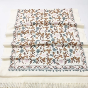 Macro detail of exquisite floral embroidery and fringe on beige cashmere-like scarf