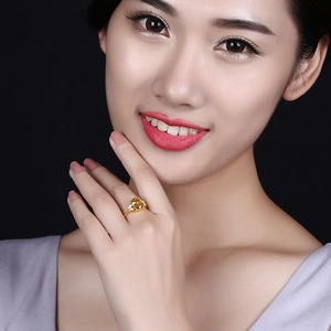 Model wearing an 18k gold plated ring with a large yellow gemstone on black background