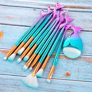 Close-up of 11 mermaid makeup brushes with fishtail scales on a blue wood background