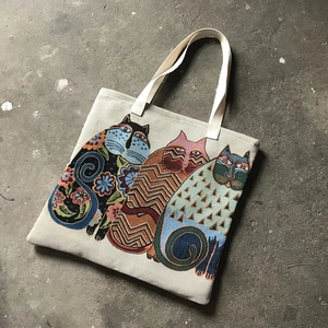 Detail of beige canvas tote bag with three stylized cats on textured ground
