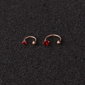 Macro shot of rose gold U-shaped ear cuffs with red zircon and metal bead on black base
