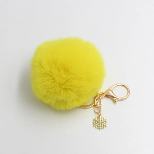 Detail van gele pluizige pompon sleutelhanger met gouden sneeuwvlok en karabijnsluiting