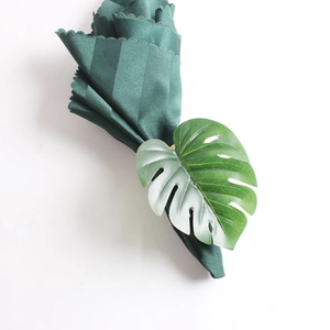 Green monstera leaf napkin ring with striped cloth on a clean white background