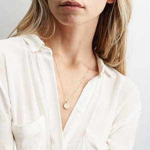 Close-up of a gold-plated hammered disc pendant necklace worn on a female neck