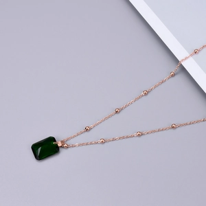 Detailed macro of emerald-cut green gemstone pendant with rose gold beaded chain
