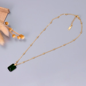 Rose gold necklace with emerald-cut green gemstone and beaded chain on a minimal background
