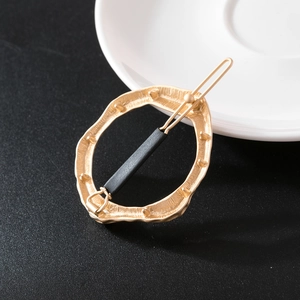 Detail of golden irregular textured alloy hair clip with brushed metal finish on dark surface
