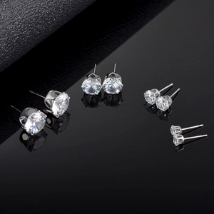 Multiple sizes of silver six-prong cubic zirconia stud earrings on a reflective black surface
