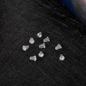 Detailed view of ten transparent silicone earring backs on a dark textured surface
