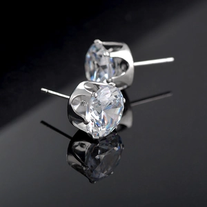 Macro shot of silver studs with clear round zircon stones on a black reflective surface