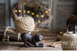 Detailed close-up of a rustic cast iron cat figurine holding a roll of natural jute twine
