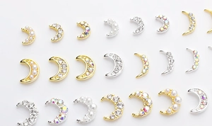 Macro detail of moon-shaped nail charms with gold and silver base and faux pearls