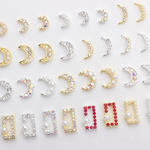 Detailed view of moon-shaped nail charms with pearls and colorful rhinestones