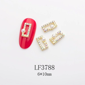 Detailed view of 6x10mm gold nail charms with AB rhinestones and pearls on red nails