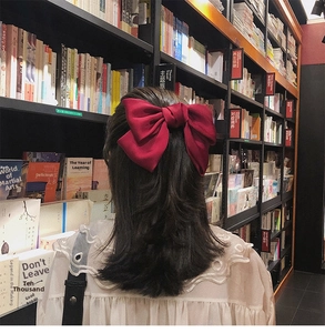 Close-up of a large red satin bow hair clip worn on wavy brown hair in a bookstore