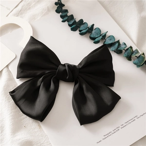 Macro shot of large black satin bow hair clip on a minimalist artistic display background