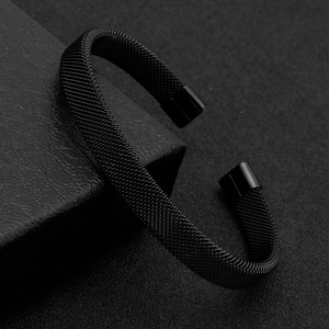 Détail d'un bracelet manchette noir en acier inoxydable sur support texturé sombre
