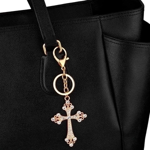 Sparkling gold cross keychain with rhinestones attached to a black leather handbag
