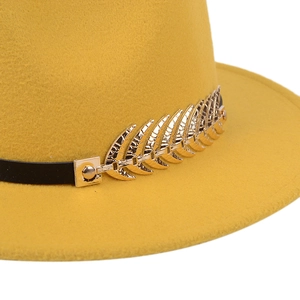Detailed close-up of golden leaf buckle on yellow wool fedora hat with black band