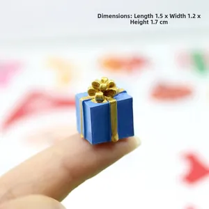 Miniature blue resin gift box with gold ribbon shown on fingertip for scale, size 1.7cm height