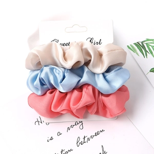 Close-up of three satin fabric scrunchies in beige, blue and pink on a retail card
