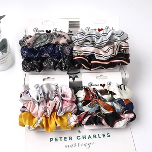 Detail view of four assorted sets of satin fabric scrunchies with floral and stripe patterns