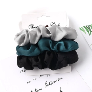 Three-piece satin scrunchies set in grey, dark green, and black on a display card