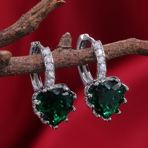 Macro shot of green heart-shaped crystal earrings hanging on a rustic wood branch