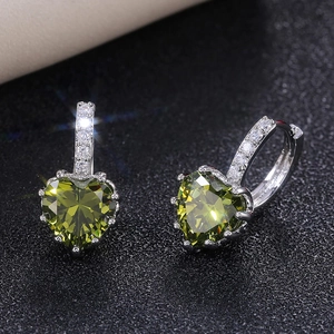Macro shot of heart-shaped emerald earrings with pavé diamond silver hooks on black base