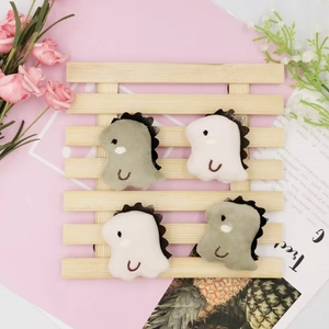 Set of four cute plush dinosaur brooches in green and white colors on a wooden tray