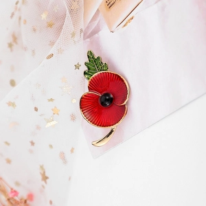Detail of red enamel poppy brooch with rhinestones on a white fabric background