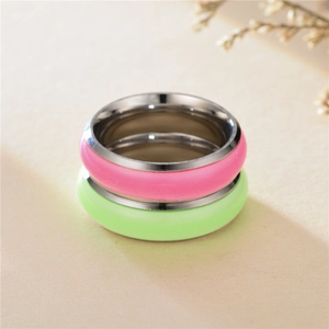 Close-up of pink and green luminous enamel stainless steel rings on a textured surface