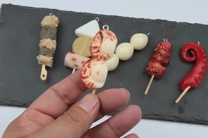 Detailed view of realistic resin food charms featuring shrimp and fish cake skewers