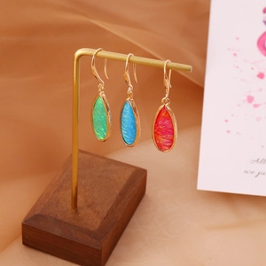 Macro detail of three colorful teardrop earrings on a gold display stand with satin background