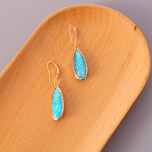 Detail of bohemian gold drop earrings with teardrop blue opal on a wood tray