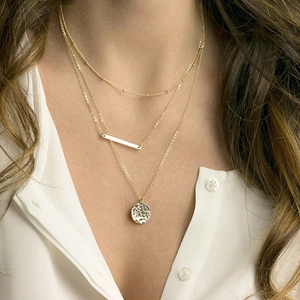 Model wearing a layered gold necklace with bar pendant and hammered coin disc charm