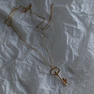 Detail shot of vintage golden key pendant on a fine cross chain over art paper