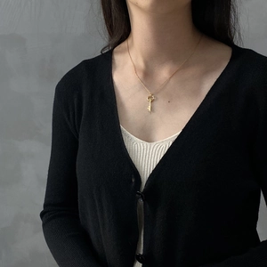 Close-up of a minimalist gold key pendant necklace worn on a model against a grey background