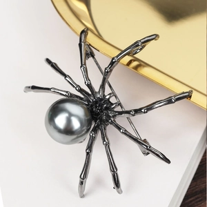 Vintage black spider brooch with grey pearl inlay on a gold and white background